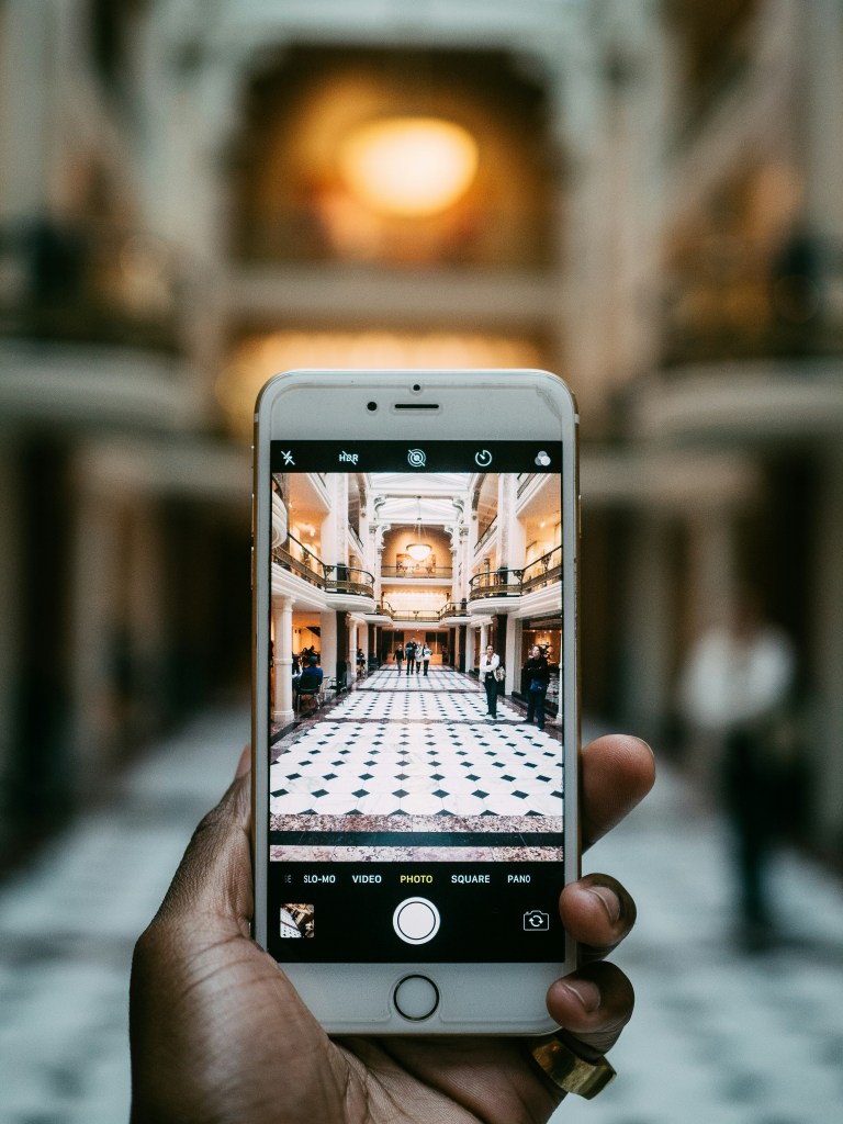 A hand holding a phone with a high contrast image of a white checked floor on it.